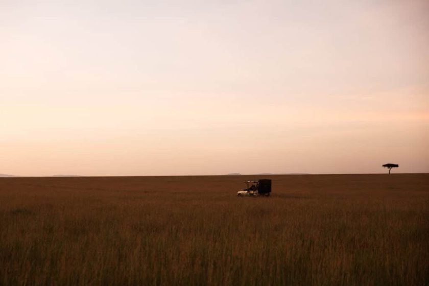 A lone safari vehicle on the open savanna at dusk